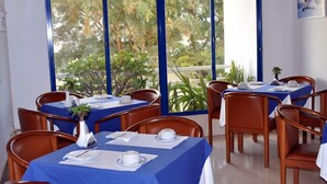 A dining area with tables set for two, blue tablecloths, white plates, and a vase with a plant. - Almar Hotel Apartamento (Albufeira)
