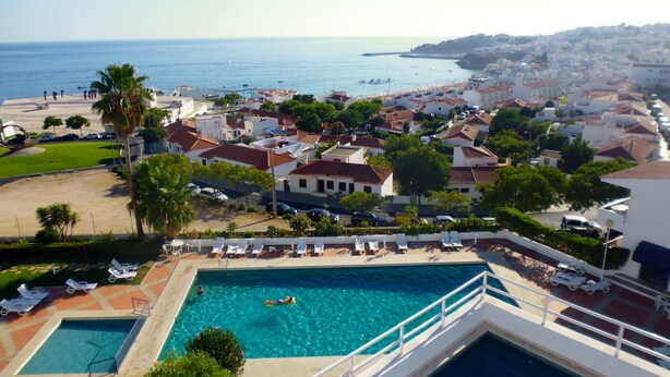 A resort with a swimming pool, lounge chairs, and a view of the sea. - Almar Hotel Apartamento (Albufeira)