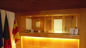 A reception desk with a warm light, flags, and a framed certificate on the wall. - Almar Hotel Apartamento (Albufeira)