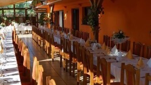 Un'ampia sala da pranzo con tavoli apparecchiati per diversi ospiti, sedie in legno e pavimento piastrellato.