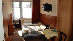 Una stanza piccola e luminosa con un letto, una scrivania, una sedia, un televisore e una finestra con tende.