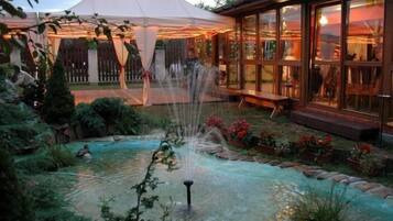 A garden with a fountain, a wooden deck, and a building with large windows.