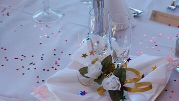 A table setting with a white tablecloth, two clear glasses, a white rose, and decorative stars and ribbons.