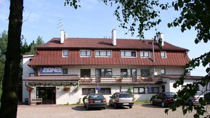 Edificio a due piani con tetto rosso, numerose finestre e un cartello con la scritta "BO". Auto parcheggiate davanti e vialetto in ghiaia.