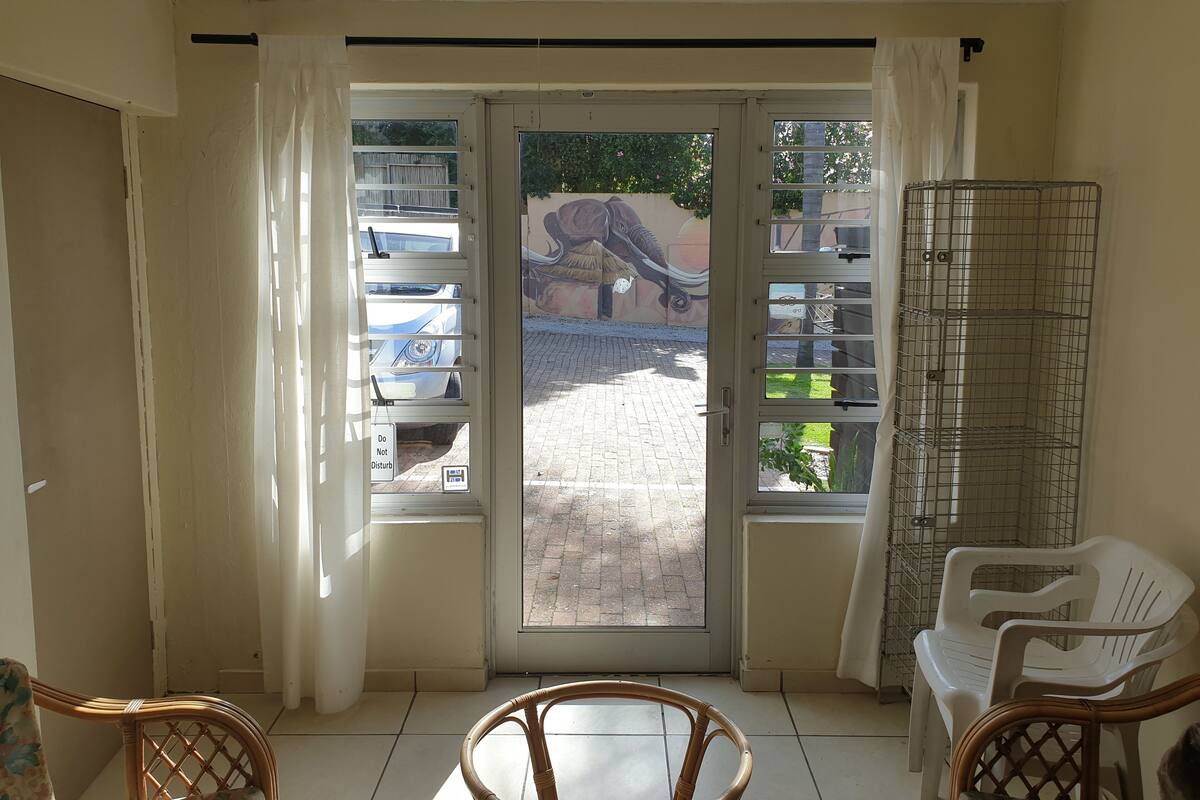 A room with a sliding glass door leading to an outdoor area, wicker chairs, a white plastic chair, and a metal rack.