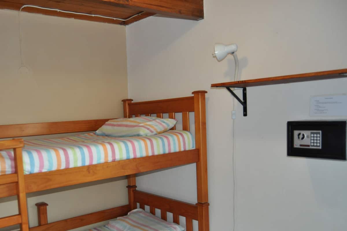 A bunk bed with a striped mattress and pillows, a white lamp on a shelf, and a security keypad on the wall.