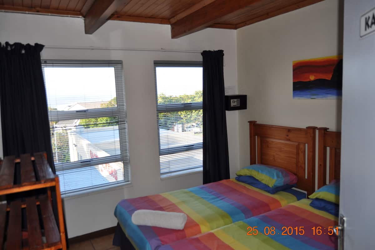 A bedroom with a bed, two windows, a painting, and a wooden headboard.