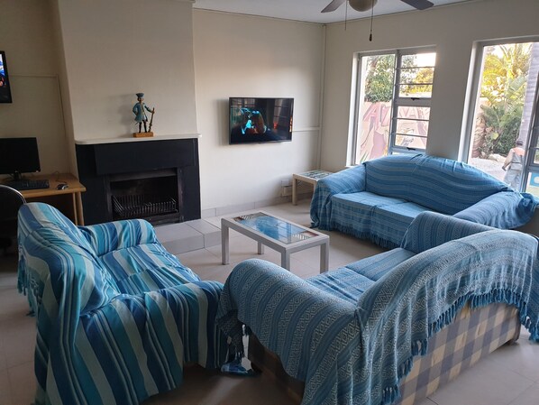 Sala de estar com móveis azuis listrados, lareira, televisão e vista para o exterior.