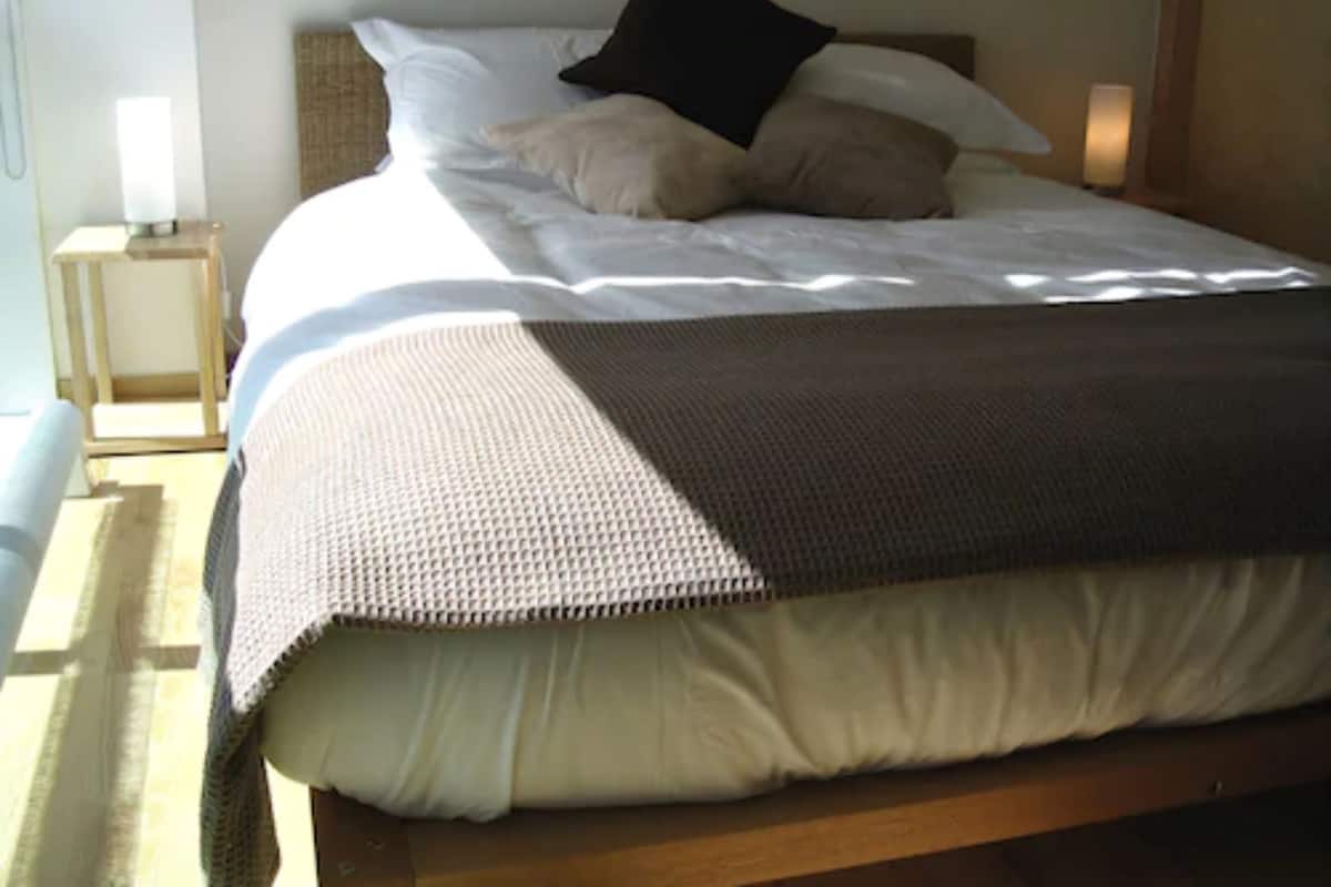 A neatly made bed with a white duvet, two pillows, and a brown throw blanket.