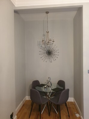 A dining area with a glass table, four chairs, and a chandelier. - Glasgow Lofts (Glasgow)