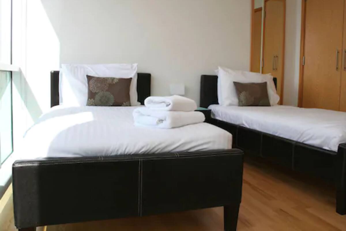 A hotel room with two single beds, a large window, and a wardrobe.