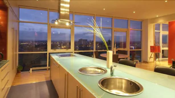 A modern kitchen with a large window, a stainless steel sink, and a view of the city at dusk. - Glasgow Lofts (Glasgow)