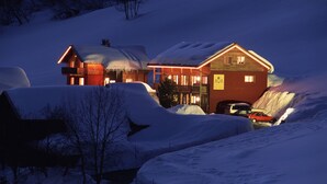 A snow-covered lodge with a warm-lit exterior, a visible signboard, and a car parked in front. - Haus Anna Apartments (Klösterle am Arlberg)