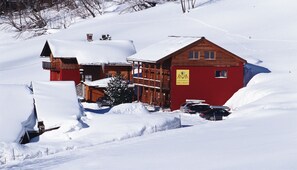 A wooden building with a red facade and a yellow sign indicating it is an apartment complex. - Haus Anna Apartments (Klösterle am Arlberg)