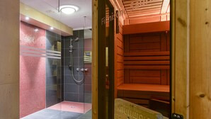 A modern bathroom with a glass shower enclosure, a wooden sauna, and a visible sign indicating the sauna area. - Haus Anna Apartments (Klösterle am Arlberg)