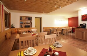 A cozy dining area with wooden furniture, a bookshelf, and a red accent wall. - Haus Anna Apartments (Klösterle am Arlberg)