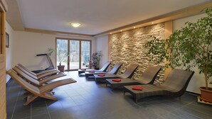 A sunlit room with multiple lounge chairs and a stone wall, featuring a large window and a potted plant. - Haus Anna Apartments (Klösterle am Arlberg)