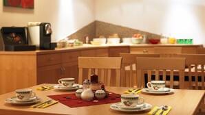A dining area with a wooden table set for tea, a coffee machine, and a fruit bowl on the counter. - Haus Anna Apartments (Klösterle am Arlberg)
