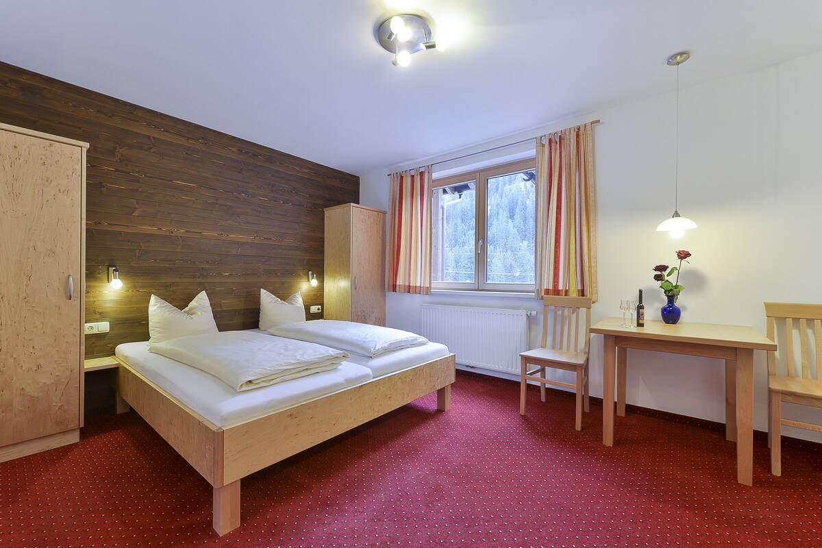 A bedroom with a wooden bed, a desk, a chair, and a window with curtains.