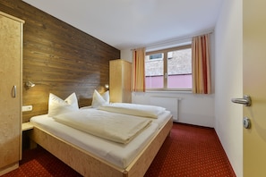 A double bed with white bedding in a room with wooden panel walls and a red carpet. - Haus Anna Apartments (Klösterle am Arlberg)