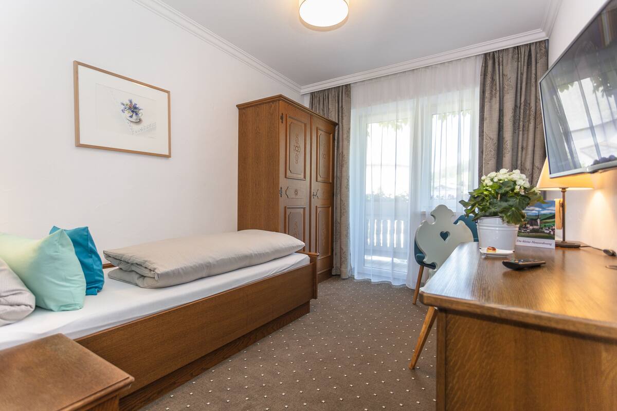 Un dormitorio con una cama individual, un armario de madera, un escritorio con lámpara y una televisión.