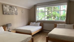 A hotel room with two single beds, a wooden floor, a large window with a view of greenery, and a wall-mounted artwork. - New Union Hotel (Manchester)