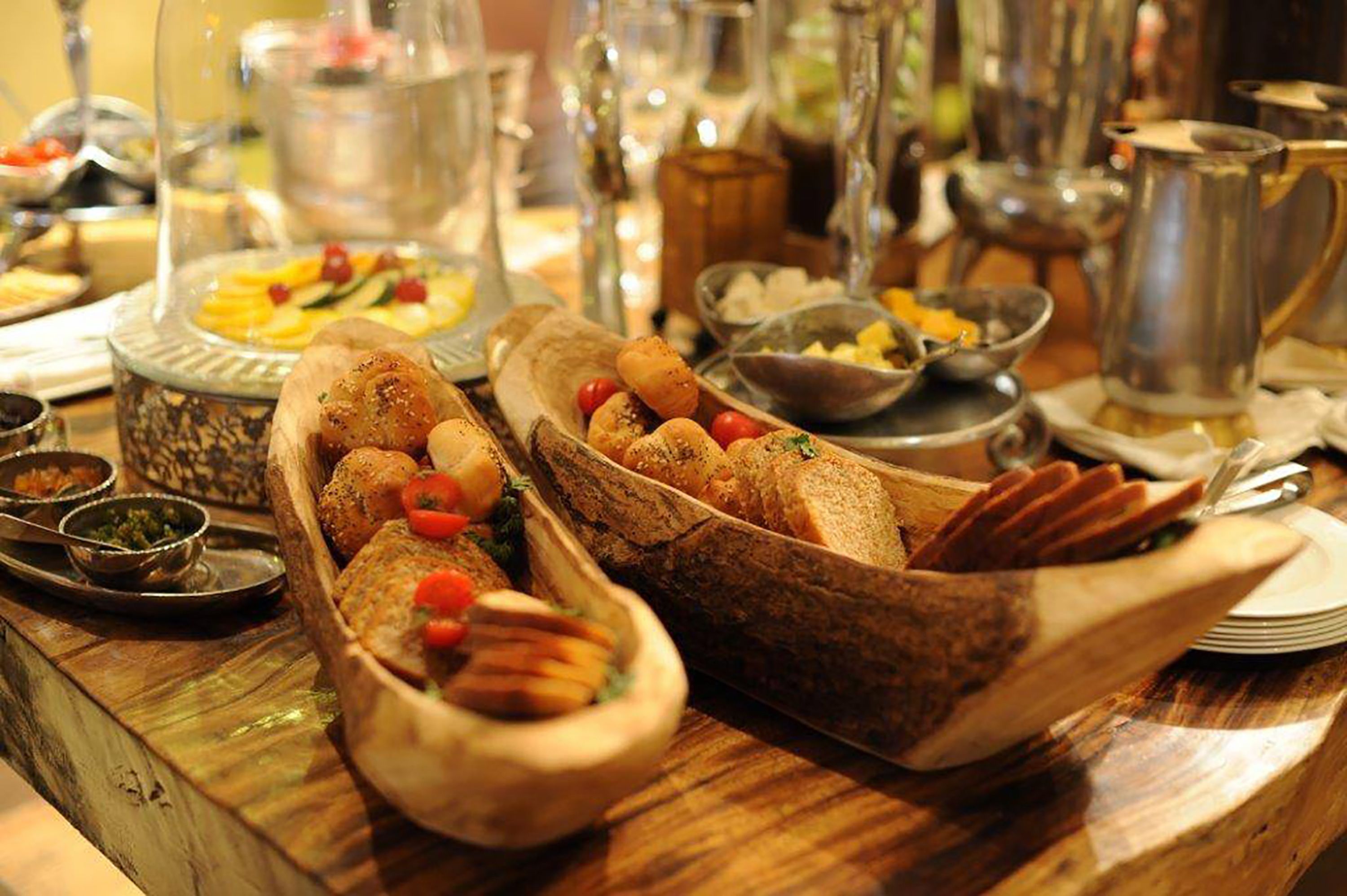 A wooden table with various dishes and utensils, including bread, vegetables, and a pitcher.