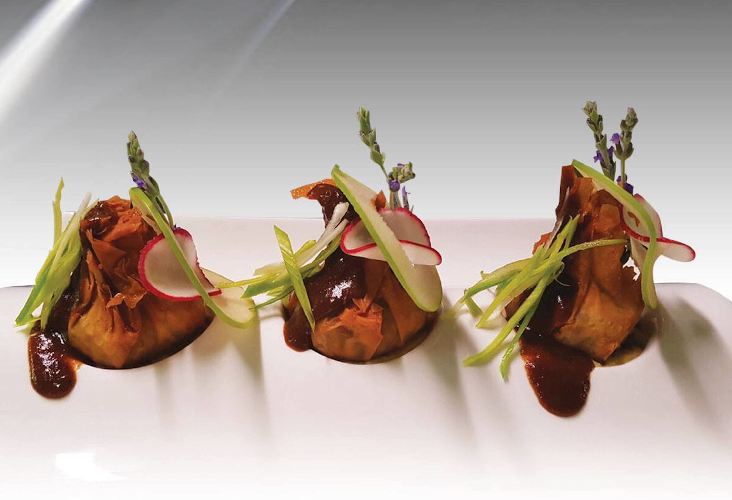 A white plate with three pieces of food, each topped with green vegetables and a small sprig of herb.
