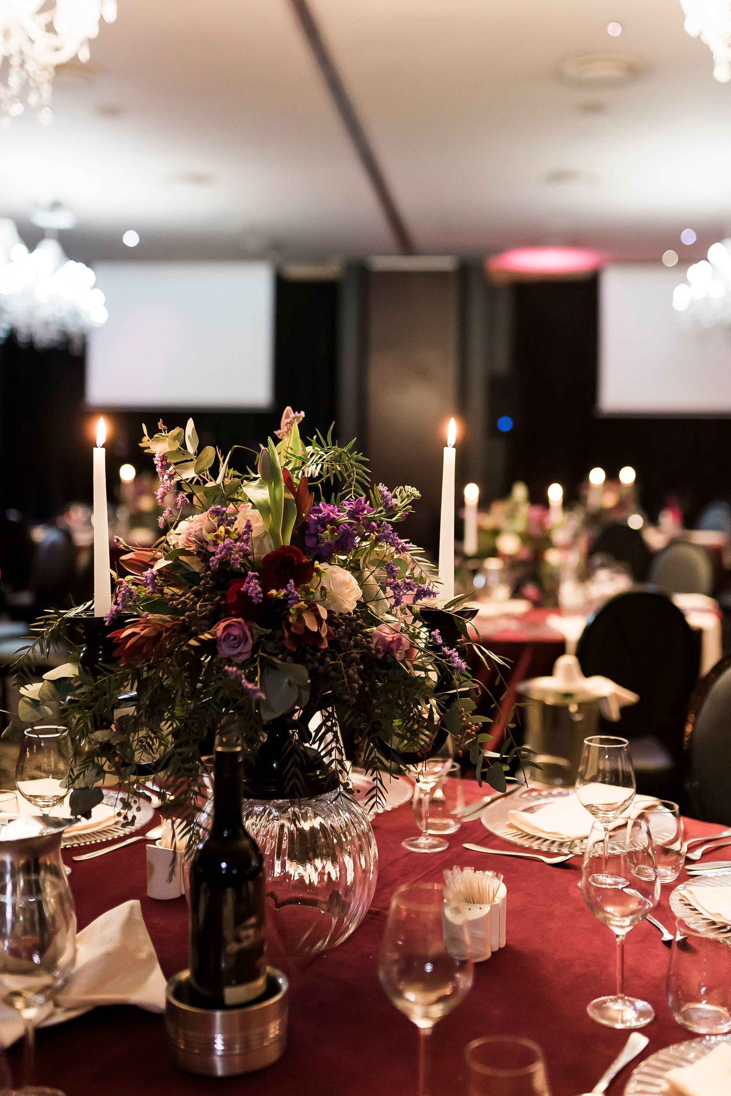 A dining table set with wine glasses, plates, and a centerpiece of flowers and candles.