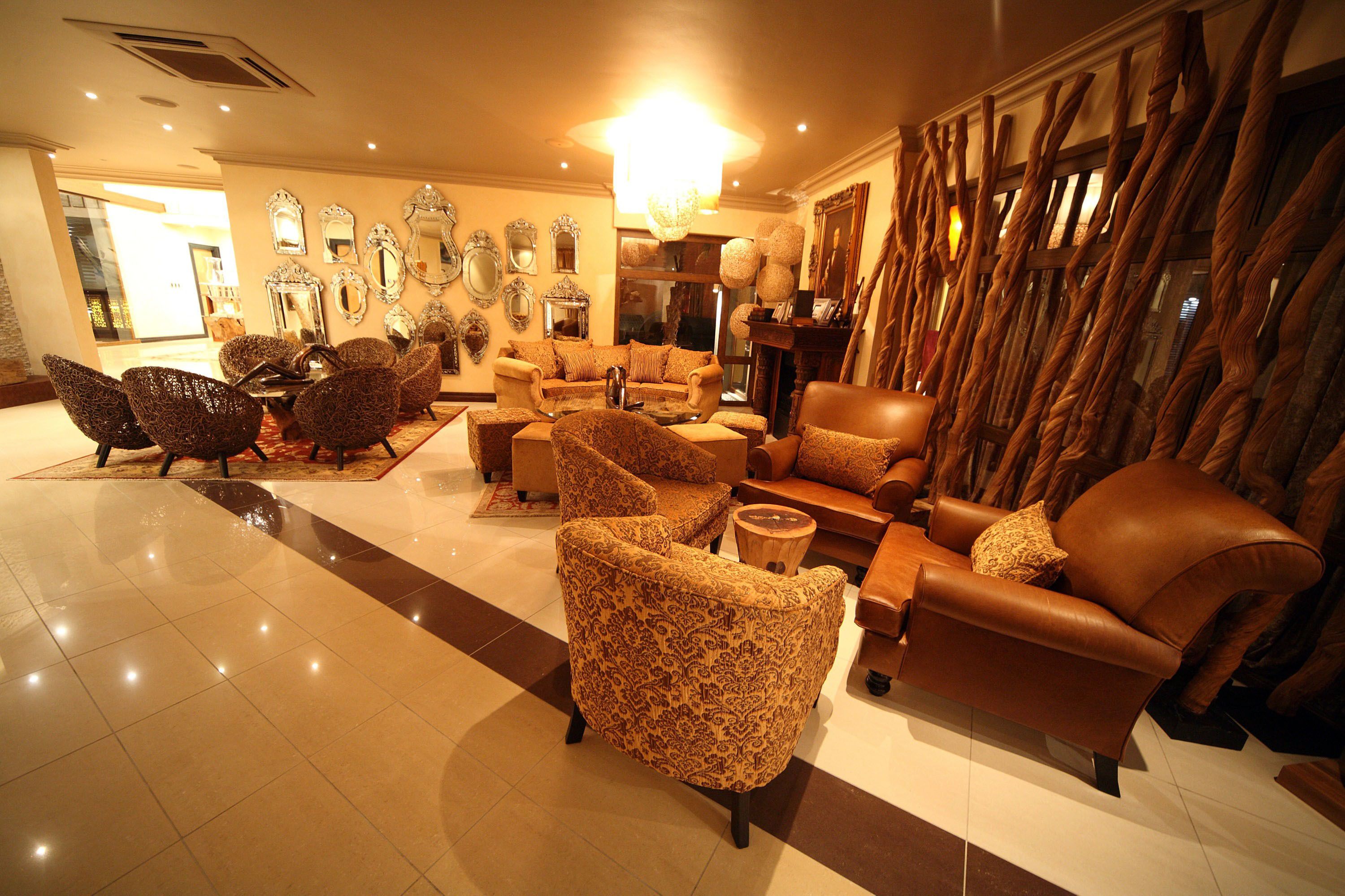 A spacious lobby with multiple seating areas, including patterned armchairs and a leather sofa, and a decorative wall with mirrors and a chandelier.