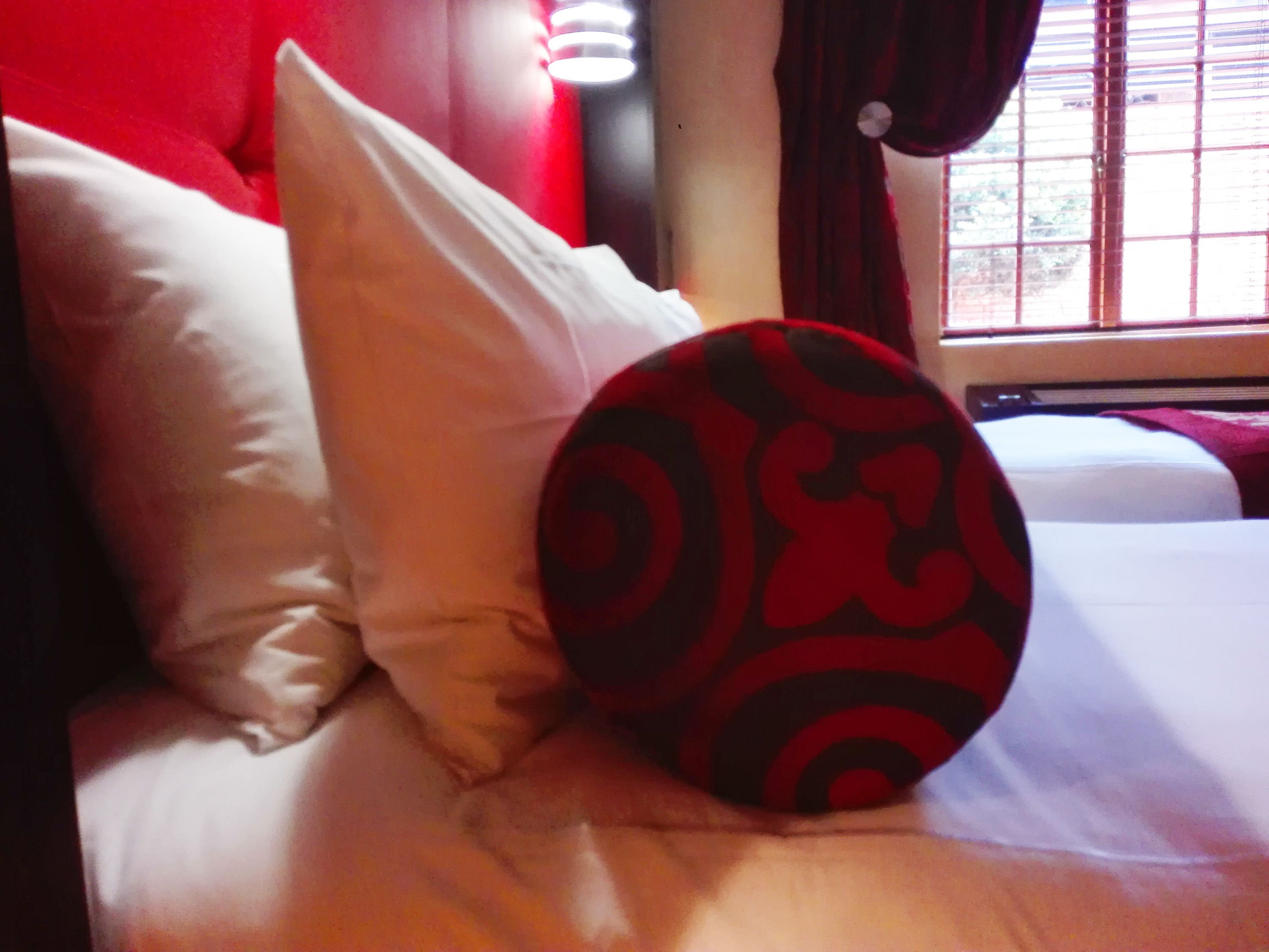 A bed with white bedding and a red and black patterned pillow.