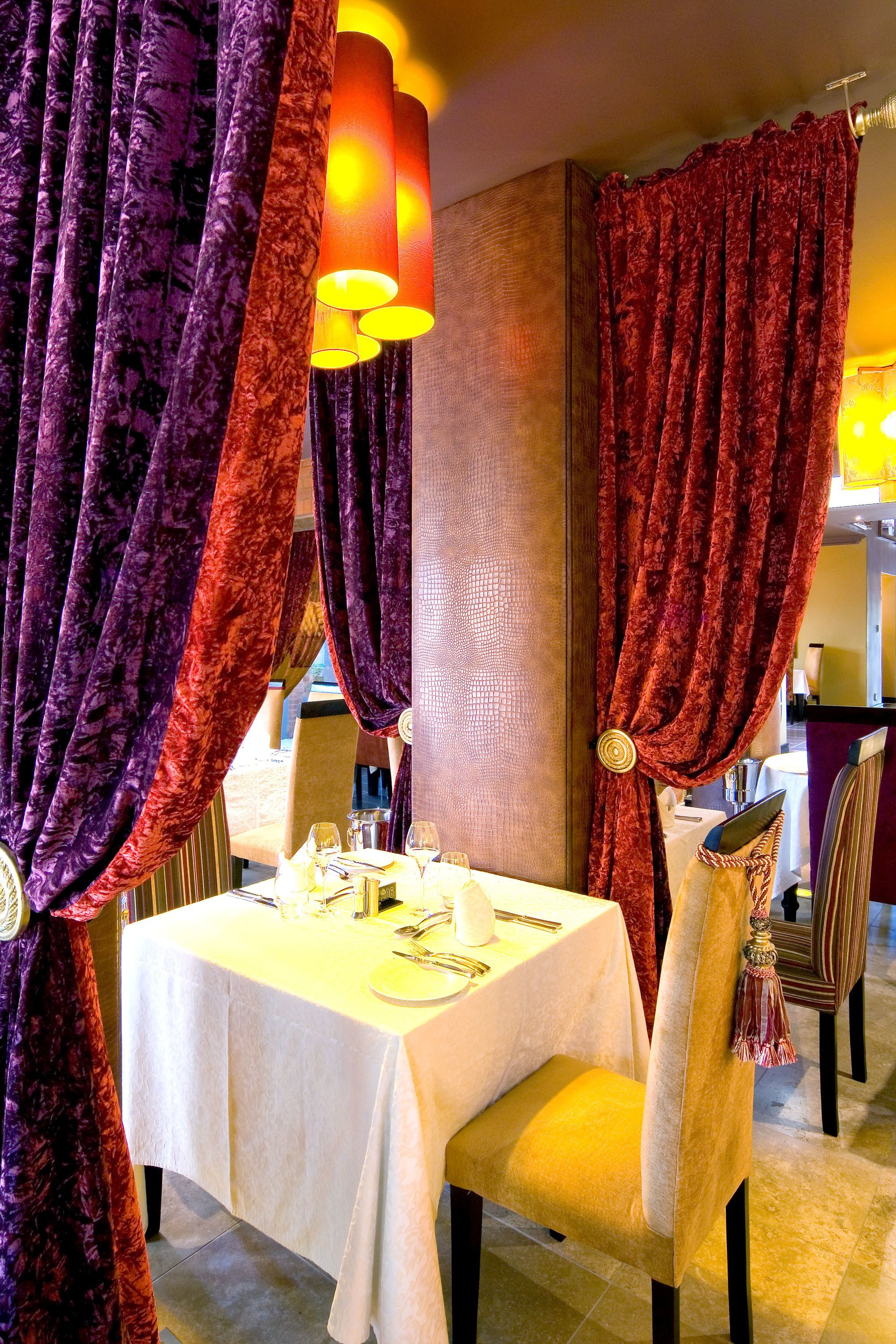 A dining area with a table set for two, draped curtains, and a chandelier.