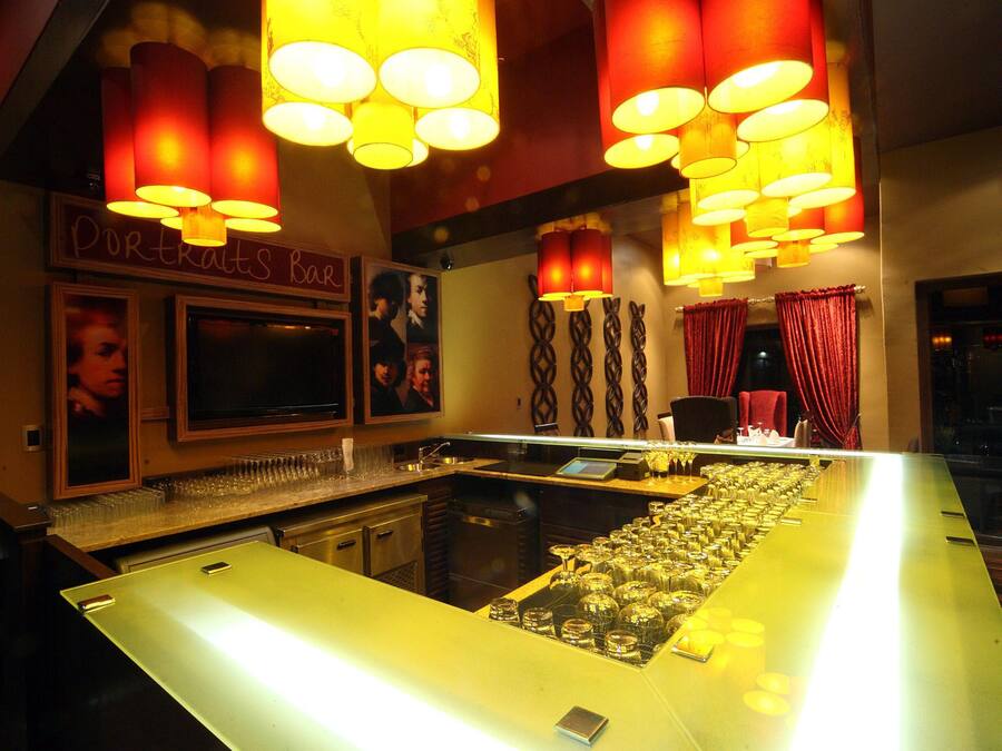 A bar area with a long counter, multiple hanging lamps, and a television screen.