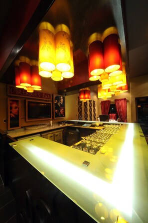 A bar area with a long counter, multiple hanging lamps, and a television screen.