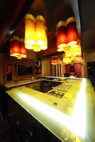 A bar area with a long counter, multiple hanging lamps, and a television screen.