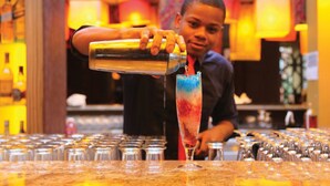 A bartender pouring a colorful drink into a tall glass.