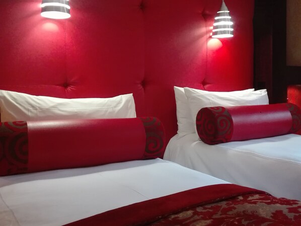 Ein Hotelzimmer mit rotem, gepolsterten Kopfteil, weißer Bettwäsche und roten Kissen mit Muster.