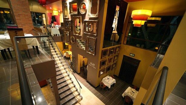 A multi-level hotel lobby with a staircase, a variety of framed mirrors, and a seating area with tables.