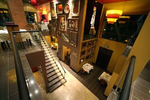 Eine mehrstöckige Hotelhalle mit Treppe, verschiedenen gerahmten Spiegeln und einer Sitzecke mit Tischen.