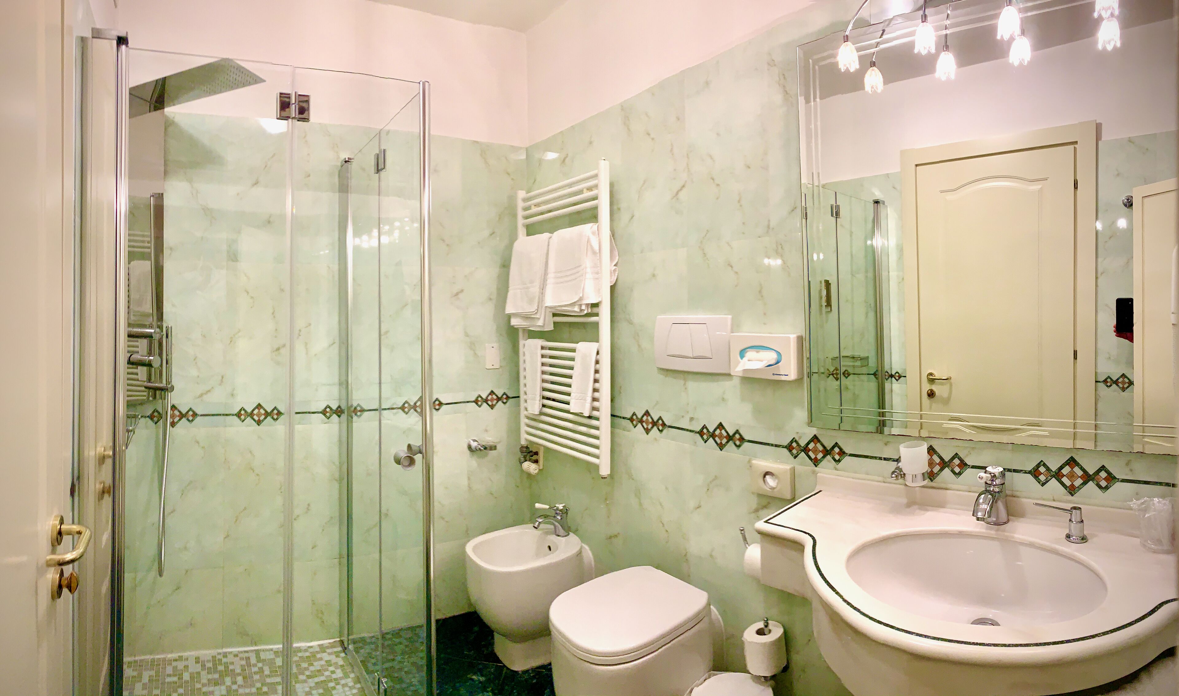 A bathroom with a glass-enclosed shower, a bidet, a toilet, a sink, and a mirror.