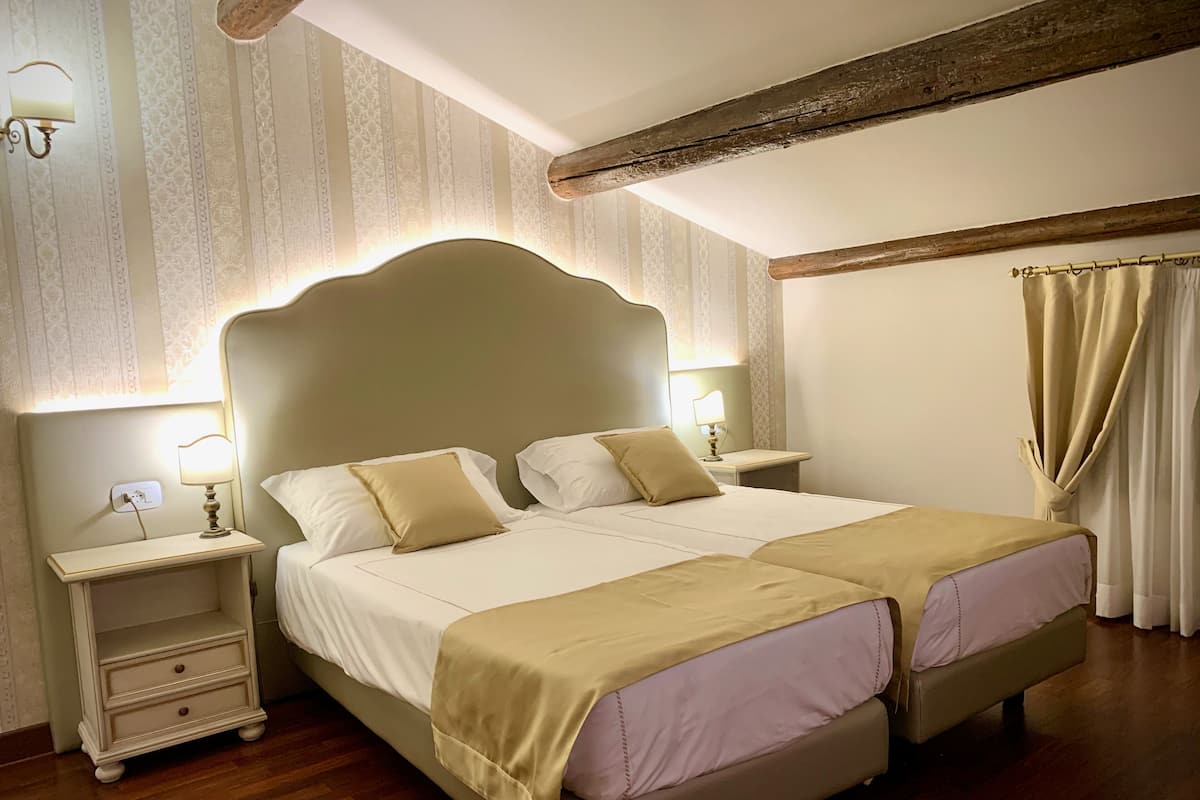 A double bed with a headboard, bedside tables with lamps, a wooden floor, and a window with curtains.