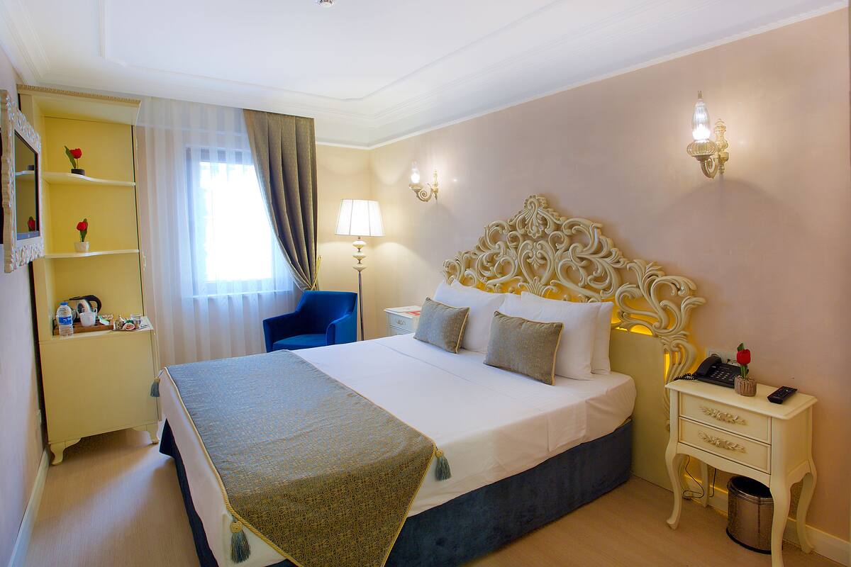 A hotel room with a large bed, a bedside table, a nightstand, a chair, a desk, and a mirror.