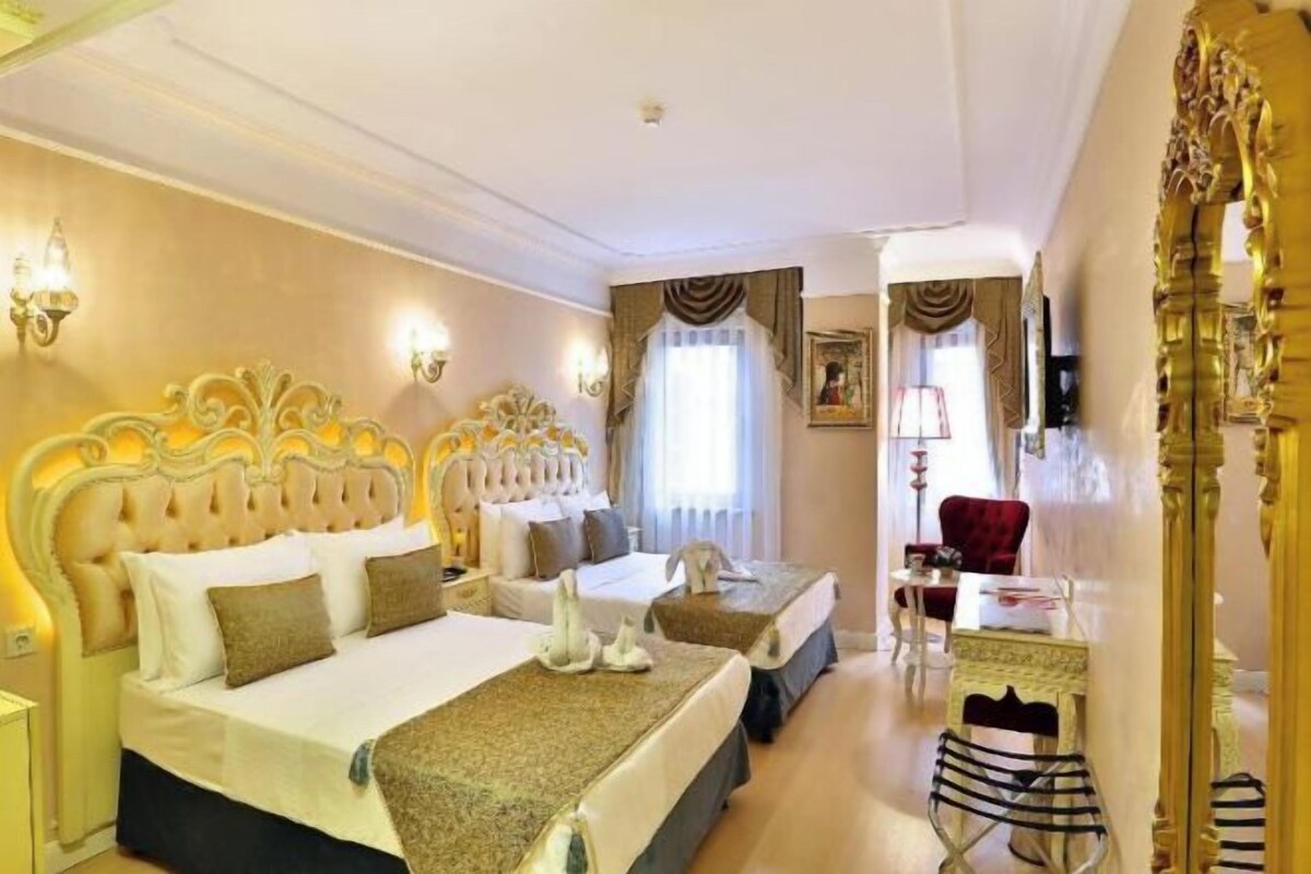 A hotel room with two beds, a sitting area with a red chair, and a large ornate mirror.