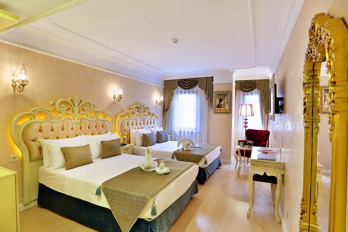 A hotel room with two beds, a red chair, a small table, and a large mirror.