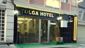 The exterior of the Tolga Hotel with a glass facade, a green awning, and a potted plant in front. - Tolga Hotel (Istanbul)