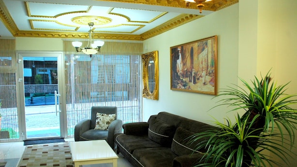 A living room with a sofa, a coffee table, a chair, a large plant, and a painting on the wall. - Tolga Hotel (Istanbul)