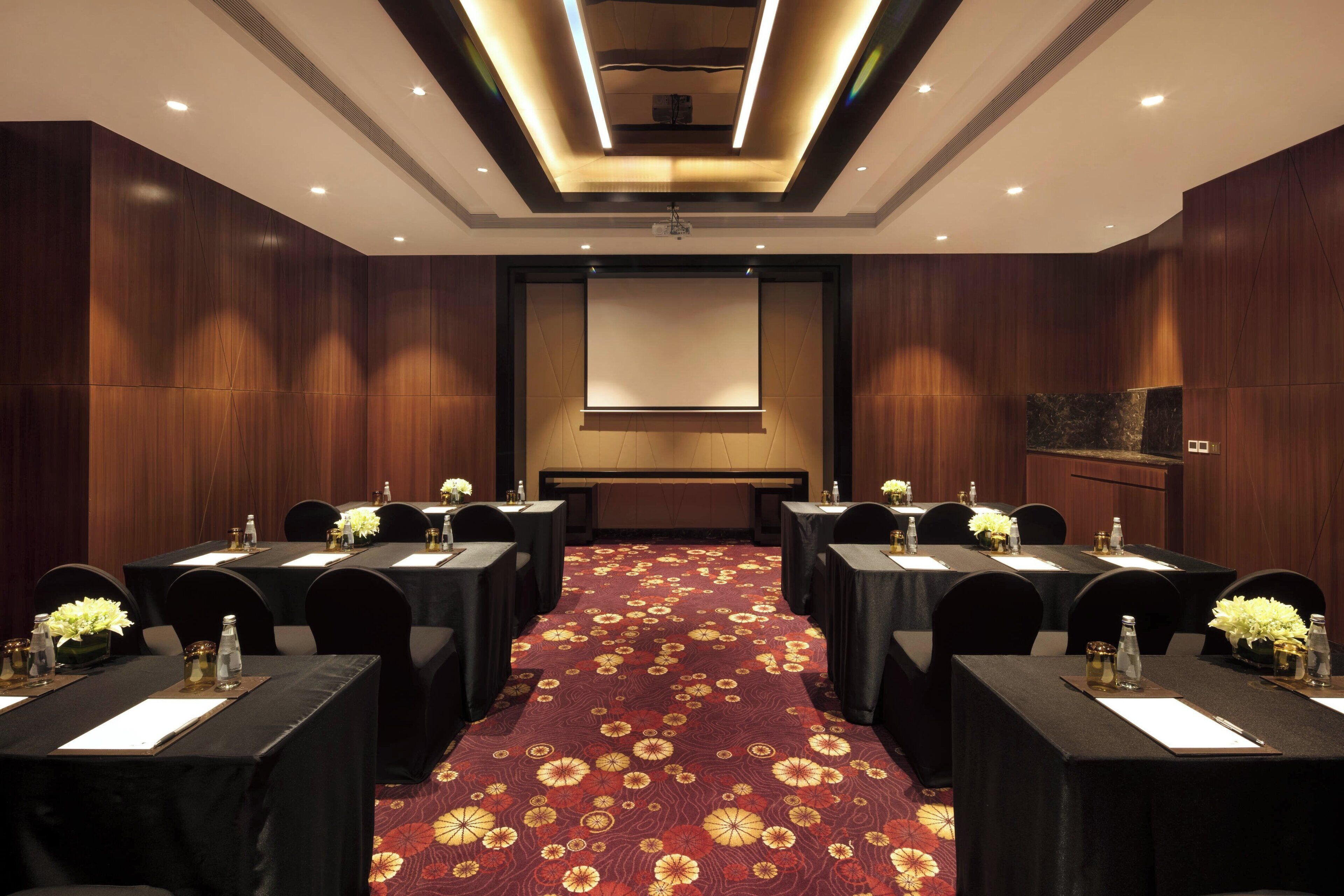 A conference room with a red carpet, multiple tables, and chairs, equipped with water bottles and nameplates.