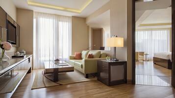 Una habitación de hotel moderna con una mesa de centro de vidrio, un sofá, una cama y una mesita de noche con una lámpara.