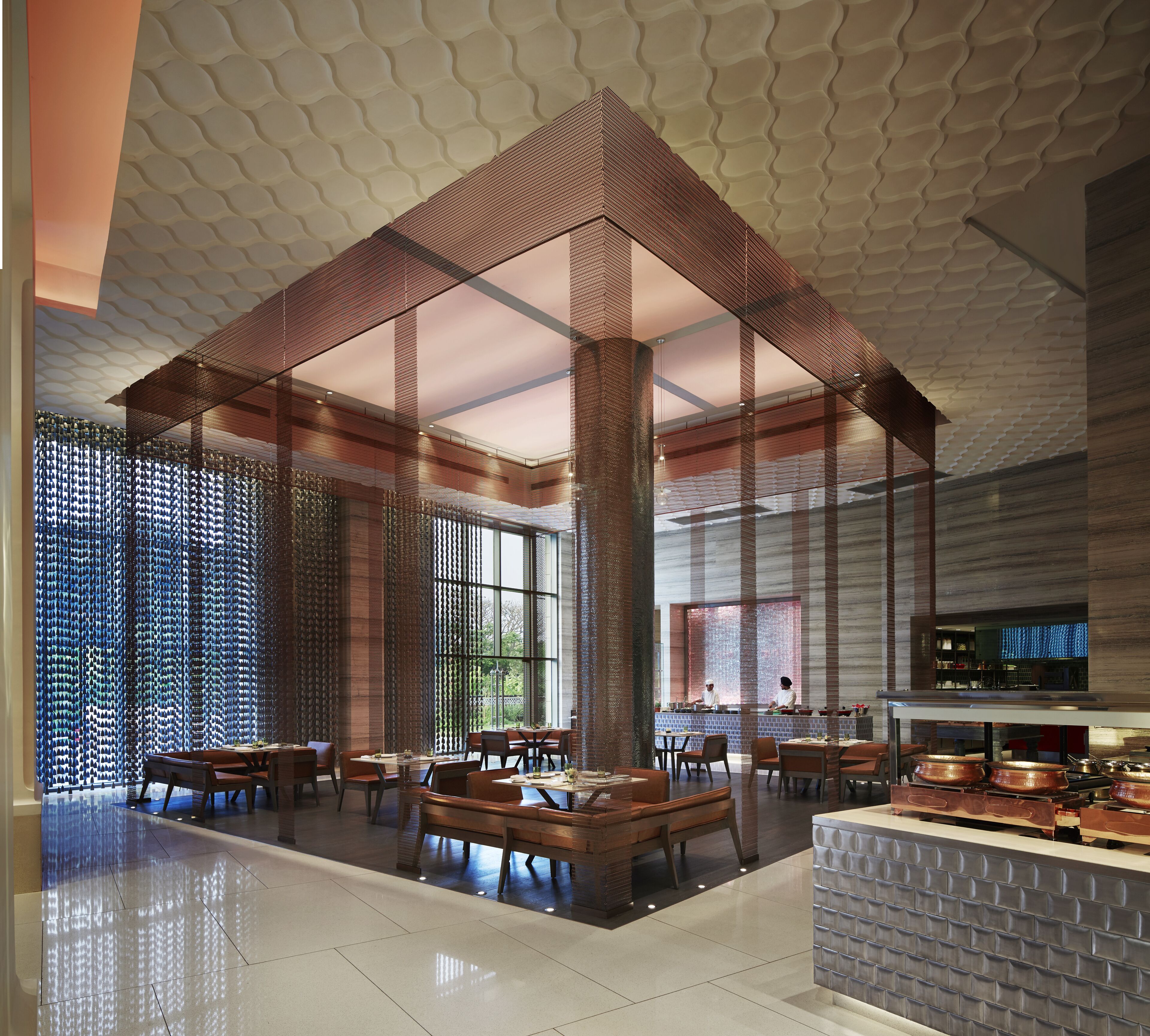 A modern restaurant interior with a high ceiling, wooden beams, and a central seating area with tables and chairs.