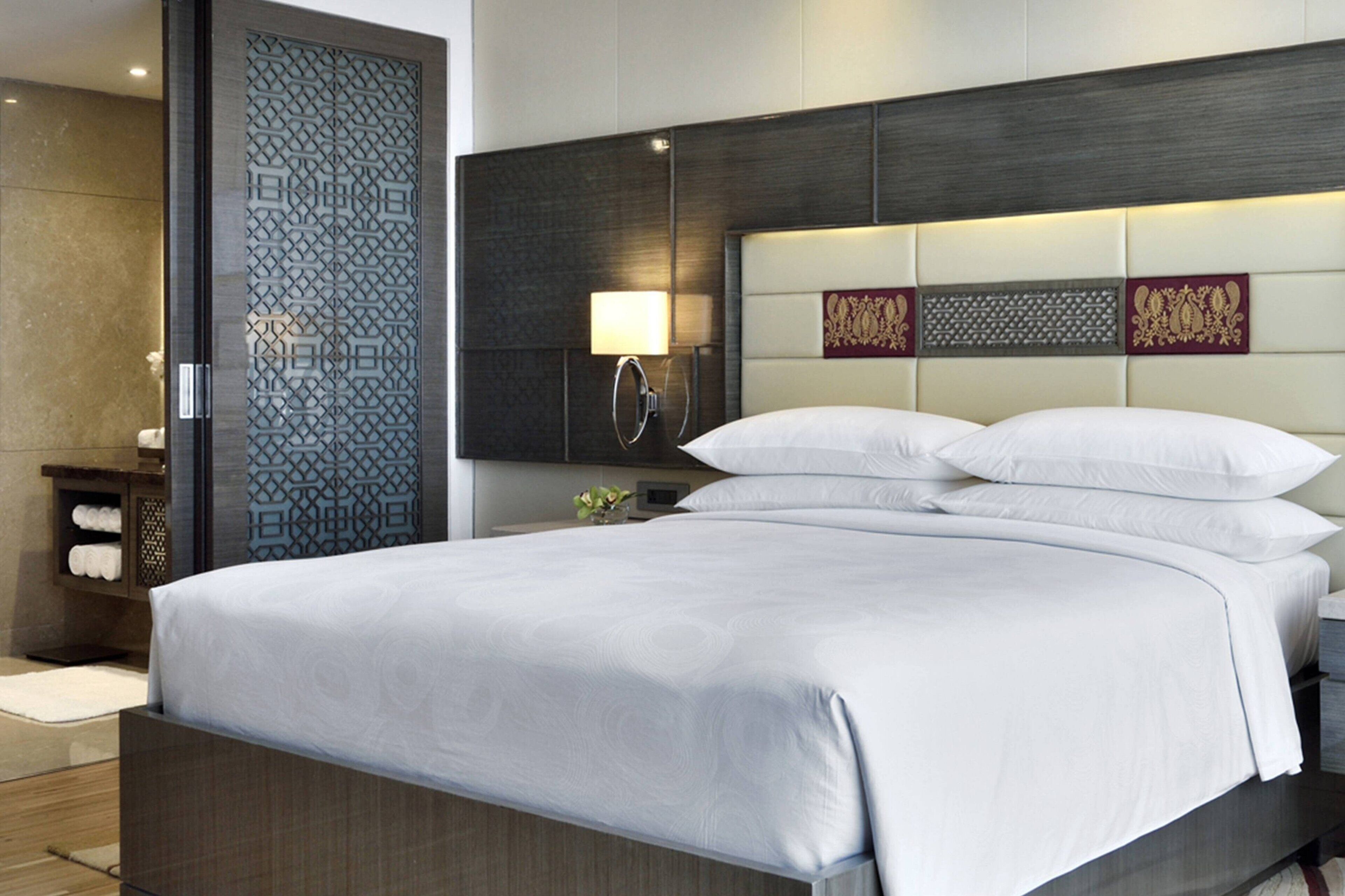 Une chambre d’hôtel moderne, dotée d’un grand lit, d’une table de chevet, d’une petite table, d’une lampe fixée au mur et de panneaux décoratifs.
